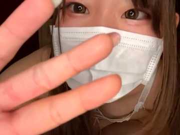 Media: Video of a woman with light skin, long brown hair, and brown eyes wearing a white medical mask, held in place by a man's hand.