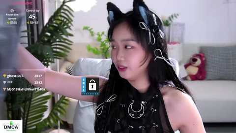 Media: Video of an East Asian woman with long black hair, wearing a black cat costume, sitting on a couch with a plush toy.