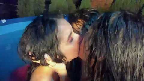 Media: Video of a close-up kiss between two women with wet, dark hair, in a swimming pool under dim lighting.