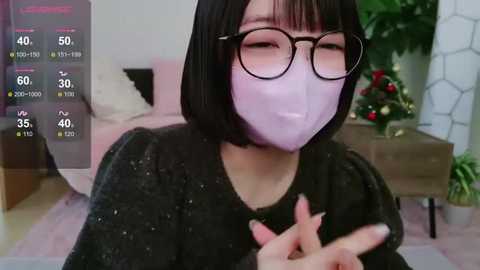 Media: A video of an Asian woman with short black hair and glasses, wearing a face mask, sitting on a sofa in a living room.