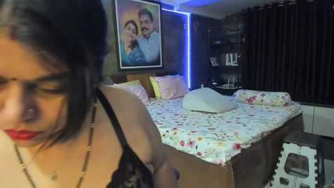 Media: Video of a dimly lit bedroom with a young woman in glasses and floral-patterned pajamas, holding a white pillow. A framed photo of a couple hangs on the wall.