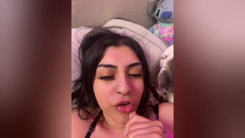 Media: A video of a young woman with medium-length black hair, wearing a black bra, lying on a bed, making a kissy face.