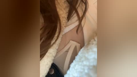 Media: Video of a woman's upper body, focusing on her cleavage. She has light skin and long, wavy brown hair. She wears a beige bra and a fuzzy, light-colored sweater.