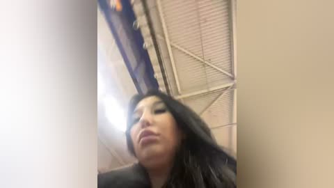 Media: A blurred video of a woman with long black hair, wearing a black jacket, taken from a low angle in a dimly lit room with metal ceiling panels.