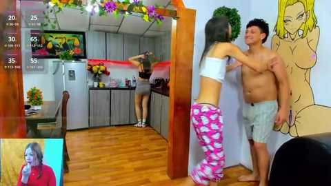 Media: A video captures a young woman in pink pajamas and a man in grey shorts, standing in a kitchen adorned with colorful art and a TV displaying an anime character.