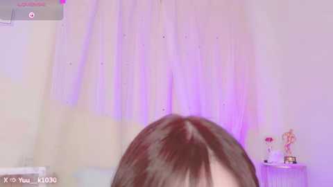 Media: A video captures a close-up of a woman's brown hair, with soft purple lighting on a white wall adorned with a small, delicate lamp.