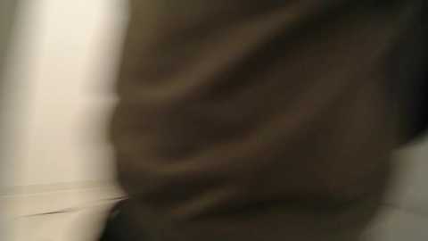 Media: A blurry video featuring a person's hand and part of their leg, wearing dark clothing, against a plain, light-colored background. The image is out of focus, making details indistinct.