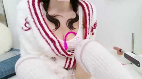 Media: Video of a woman in a white robe with red stripes, wearing white knee-high socks and a pink bra, holding a pink vibrator.