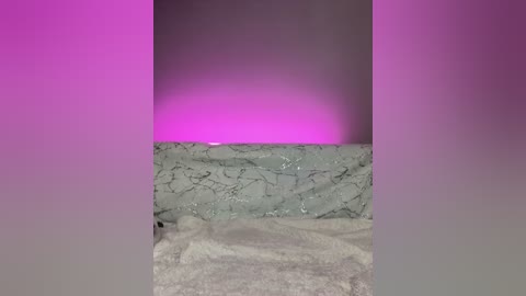 Media: Video of a bathroom with a marble-tiled wall and countertop, illuminated by a pink light, creating a soft glow. The counter is cluttered with a towel and toiletries.