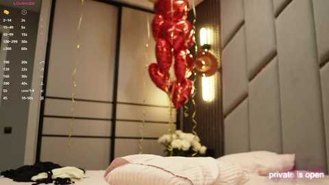 Media: Video of a cozy bedroom with a red heart-shaped balloon, white bedding, and a soft, warm light. A digital screen displays \"Live\" and a clock, indicating a streaming platform.