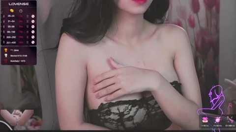 Media: A video of an Asian woman with long black hair and fair skin, wearing a black lace strapless dress, covering her breast. Background includes a bedroom setting with a bed, a purple and pink floral patterned wall, and a \"LOUNGE\" overlay.