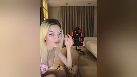 Media: A video of a blonde woman with fair skin, wearing a pink bra and leopard print shorts, crouched in a hotel room, holding a gaming controller.