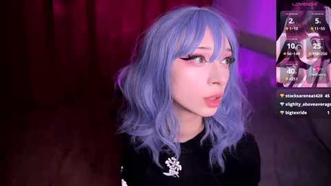 Video of a young woman with wavy, light blue hair, wearing a black sweater with white snowflakes, in a dimly lit room. Social media statistics display in the corner.