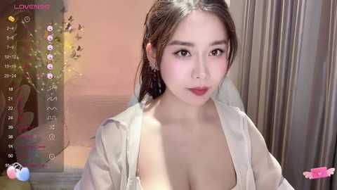 Media: A video of an East Asian woman with fair skin and dark hair, wearing an open white shirt, taken indoors with a digital overlay of a live stream interface.