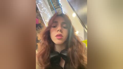 Media: Video of a young woman with long, wavy brown hair, wearing a black leather jacket, and standing in a brightly lit, modern interior.