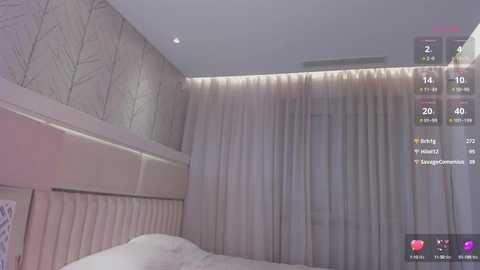 Media: Video of a modern bedroom featuring a padded headboard, light beige walls, and sheer curtains. The room is illuminated by ambient lighting. A virtual reality interface overlays the scene, displaying user information.