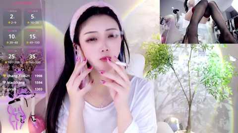 Media: Video collage featuring an East Asian woman with long black hair, wearing a pink headband, white top, and pink nails, blowing a vape. Background includes green plants and a digital clock.