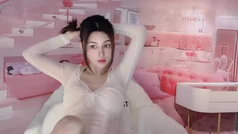 Media: Video of an Asian woman with medium skin tone, long dark hair, and fair complexion, sitting on a white bed, dressed in a white blouse and robe, against a pink, soft-focus bedroom backdrop.