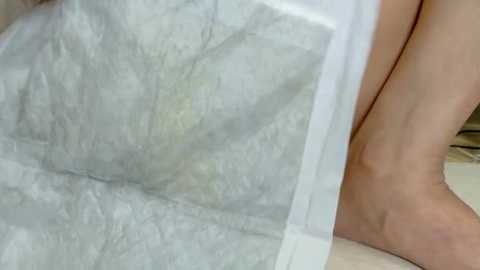 Media: A close-up video of a person's leg, partially covered by a white, crinkled fabric, possibly a blanket, against a light-colored background. The skin tone is light, and the texture of the fabric is smooth but slightly wrinkled.