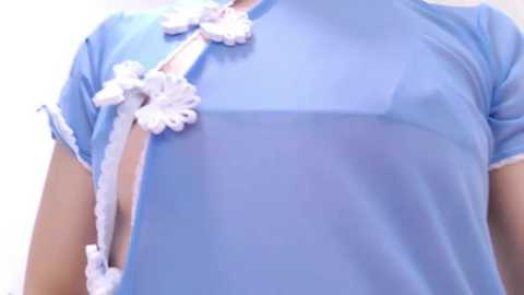 Media: Video of a person wearing a sheer, light blue Chinese cheongsam with white floral embroidery, featuring a high collar and a draping sash. The background is plain white.