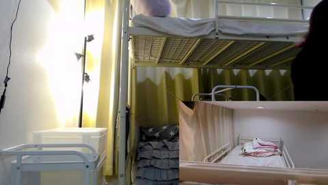 Media: Video of a minimalist hospital room with a metal-framed bunk bed and a single mattress, yellow curtains, a white cabinet, and a lamp.