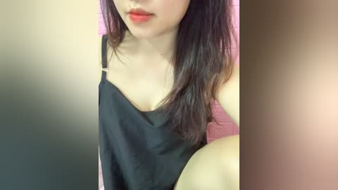 Media: Video of a young Asian woman with long black hair, fair skin, and red lipstick, wearing a black tank top. The background is blurred, with a gradient from dark to light.