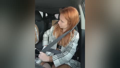 Media: Video of a blonde woman in a checkered coat, buckling her seatbelt in a car with dark interior.