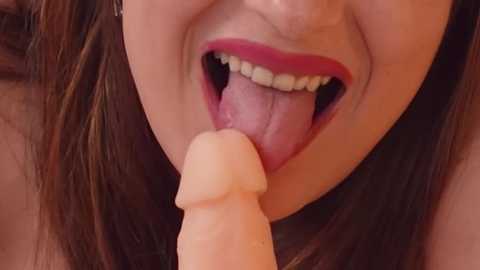 Media: Video of a woman with fair skin and red lipstick, sticking out her tongue to lick a large, lifelike pink dildo.