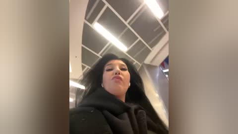 Media: A video of a young Asian woman with long black hair, wearing black clothing, captured from a low angle, indoors under fluorescent lighting.