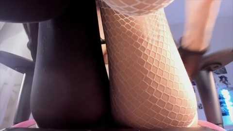 Media: A video of a woman in fishnet stockings and a sheer white top, her legs positioned closely together, creating a sensual, intimate scene. The background is blurry, with soft lighting.