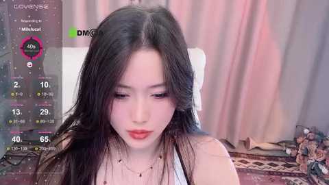 Media: A video of an Asian woman with long black hair, wearing a white top and red lipstick, sitting in a room with a TV screen showing her live stream.