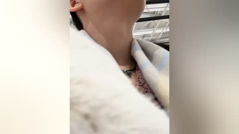 Media: Video of a person with fair skin, wearing a white, patterned scarf with pastel colors, partially covering their face. Background shows an industrial setting with metal beams and gray walls.