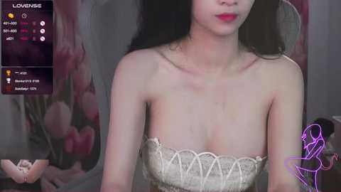 Media: A video of a fair-skinned, slender Asian woman with long black hair, wearing a strapless, lace-embellished dress, sitting against a floral-patterned backdrop.