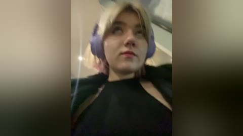 Media: A blurry video of a young woman with fair skin, wearing purple headphones, black top, and red lipstick, looking contemplative indoors.