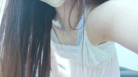 Media: A video of a woman with long, straight brown hair, wearing a white lace top, taking a selfie from an upward angle, showing her cleavage.