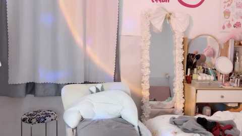 Media: A video of a cozy, pastel-colored bedroom with a white chair, fluffy white rug, white bed, and a vanity table with makeup items, adorned with a pink bow.