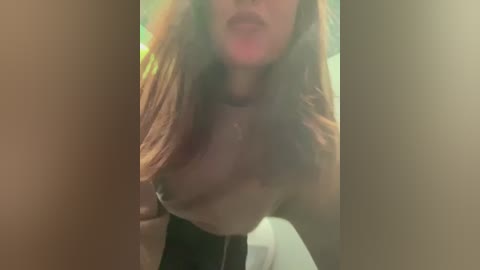 Media: A blurry video of a topless woman with medium-sized breasts and long, light brown hair, wearing a black choker necklace, taken from a low angle.