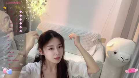 Media: A video of an Asian woman with long black hair, wearing a white top, sitting on a beige couch with a plush white bear.