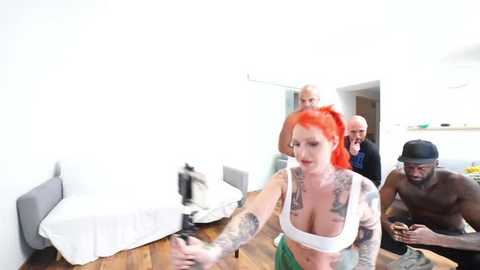 Media: A video of four people in a modern, bright apartment: a red-haired woman with tattoos, a shirtless muscular Black man, and two other men in casual clothes.