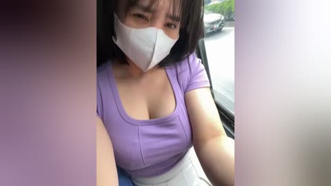 Media: A video of an East Asian woman with shoulder-length black hair, wearing a white face mask, a purple short-sleeved top, and a white skirt, seated in a car with a blurred outdoor view.