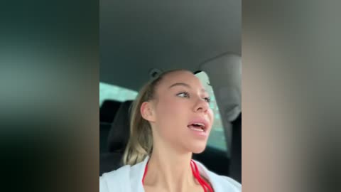 Media: A video of a blonde woman in a white lab coat, looking upward, with a blurred car interior background.