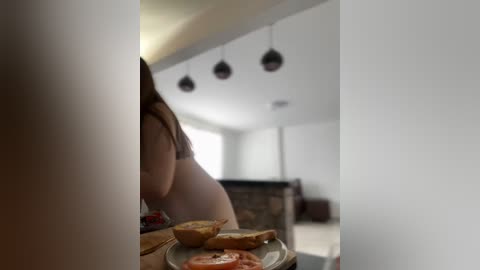 Media: A video showing a partially cropped woman in a striped bra, holding a pizza box, in a modern, minimalist kitchen with white walls and hanging pendant lights.