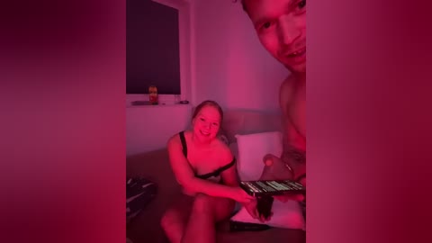 Media: A video shows a nude, smiling woman with a medium build and medium-sized breasts playing a keyboard in a dimly lit room, bathed in pink lighting.