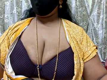 Media: Video of a woman with medium-dark skin wearing a purple bra, golden necklace, and yellow floral-patterned scarf. She has a black mask covering her mouth and nose.