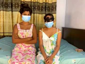 Media: Video of two young women wearing blue face masks, pink floral pajamas, and lace masks, sitting on a blue bed with striped curtains in the background.