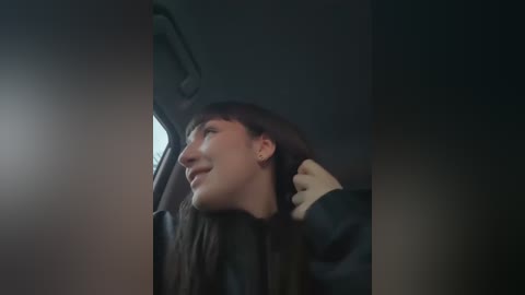 Media: Video of a young man with long brown hair, wearing a black jacket, smiling and touching his hair while sitting in a dimly lit car.