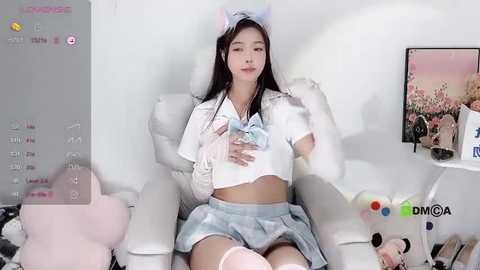 Media: Video of an Asian woman in a white furry jacket, blue plaid skirt, and pink thigh-high socks, seated on a white chair in a pastel room.