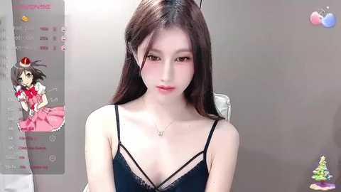 A video of a young East Asian woman with fair skin, long dark hair, and delicate features, wearing a black lace bralette, sitting indoors.