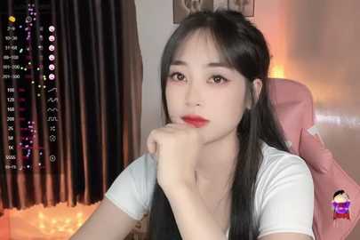 Media: A video of an East Asian woman with long black hair, fair skin, and red lipstick, sitting in a pink chair, looking contemplative. Background shows a dimly lit room with curtains and a digital clock.