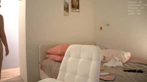 Media: Video of a messy bedroom with a white chair, pink pillows, scattered clothes, and a partially open door.